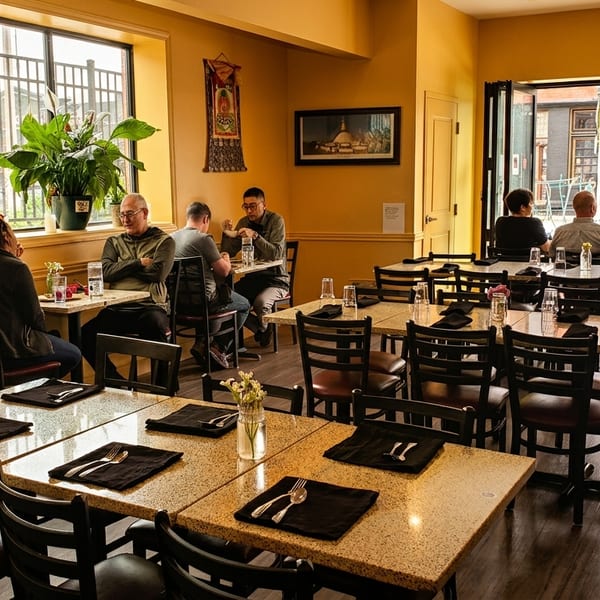 A restaurant dining room with patrons seated at tables and a server standing near an open doorway.